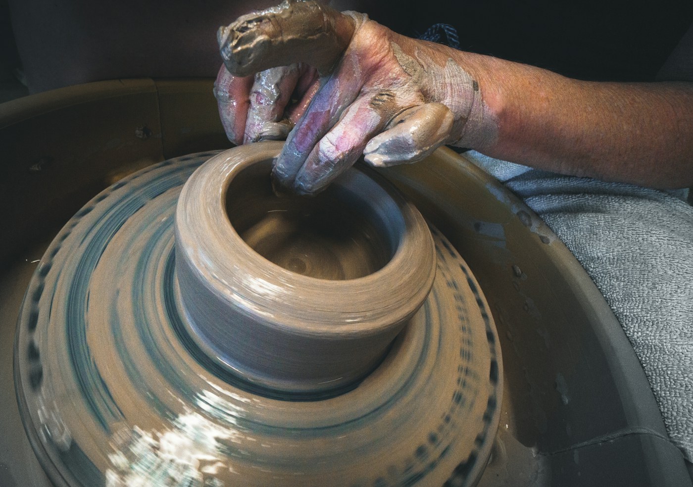 A clay-covered hand shaping a rounded vessel on a spinning pottery wheel.