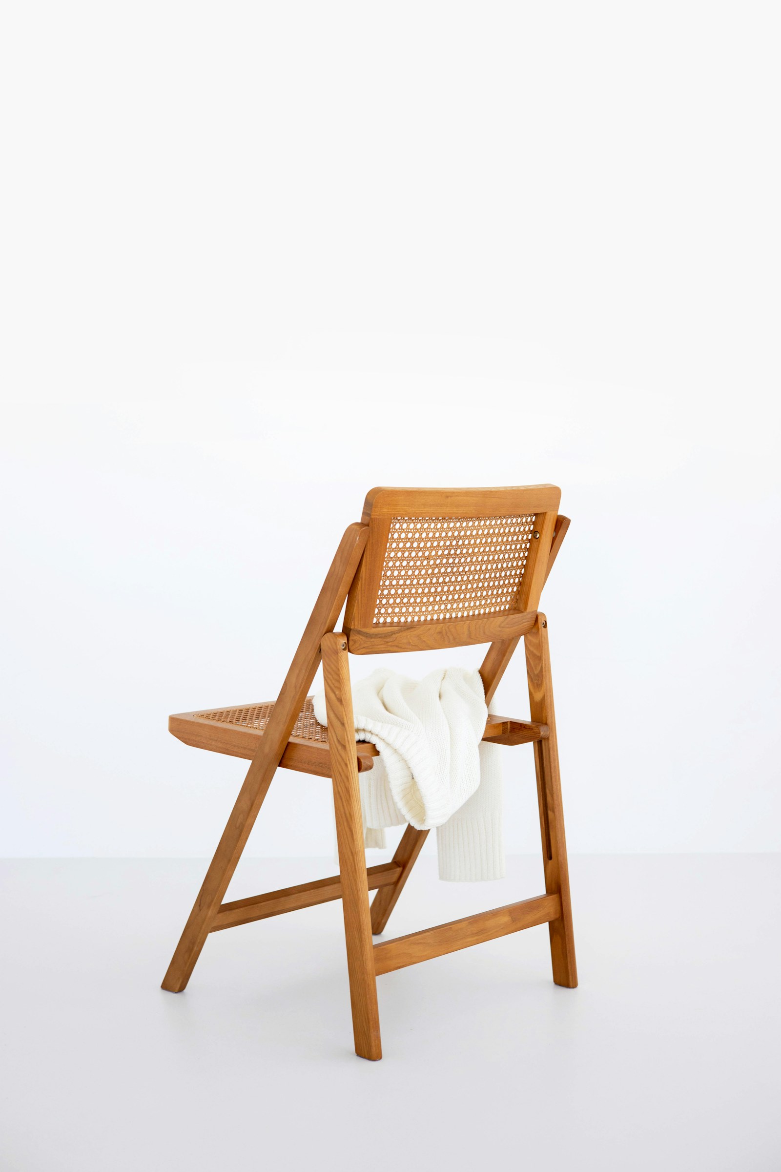 A timber chair with a woven back and seat, with a white textile draped over it.