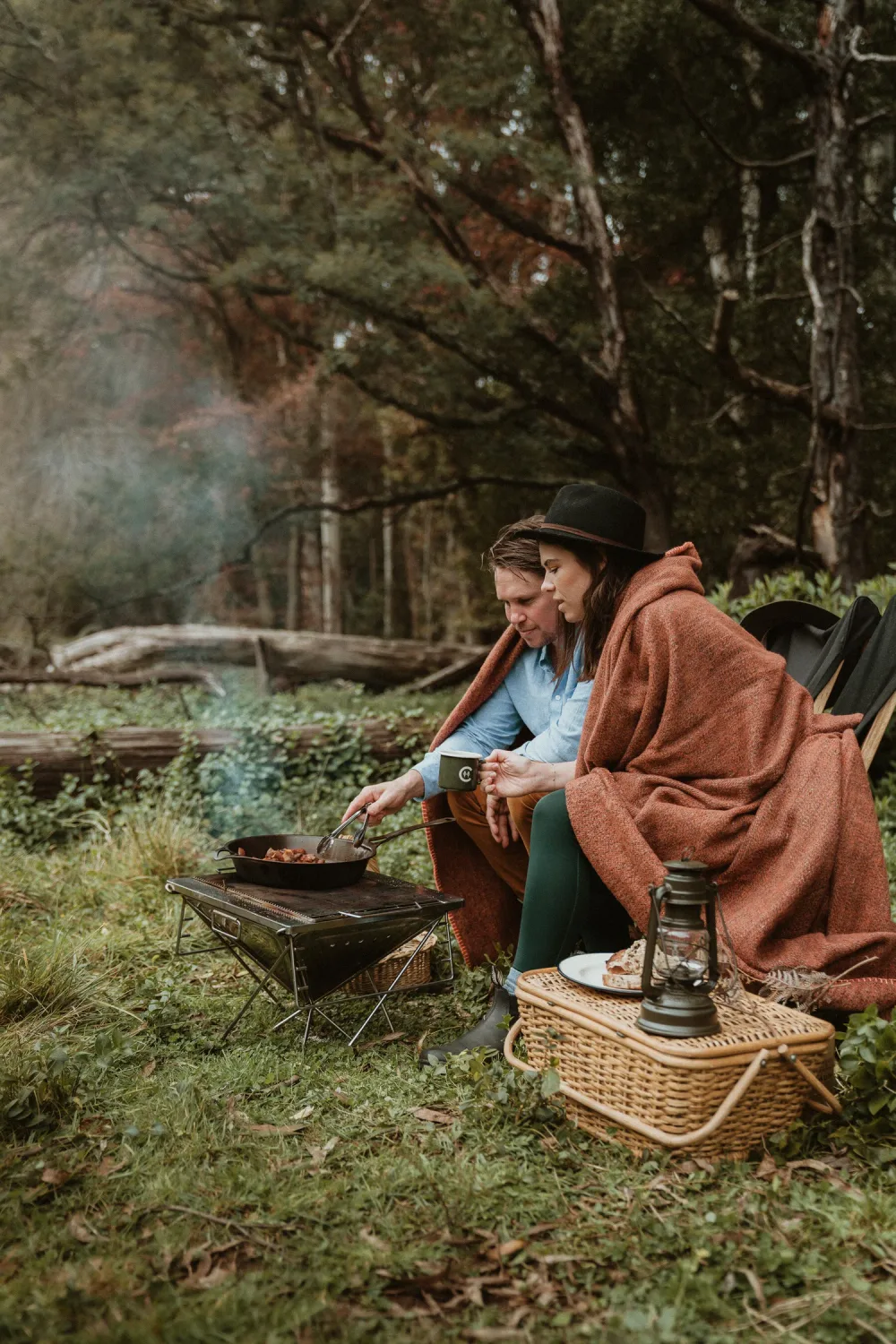 A person wrapped in a blanket beside moss and timber.