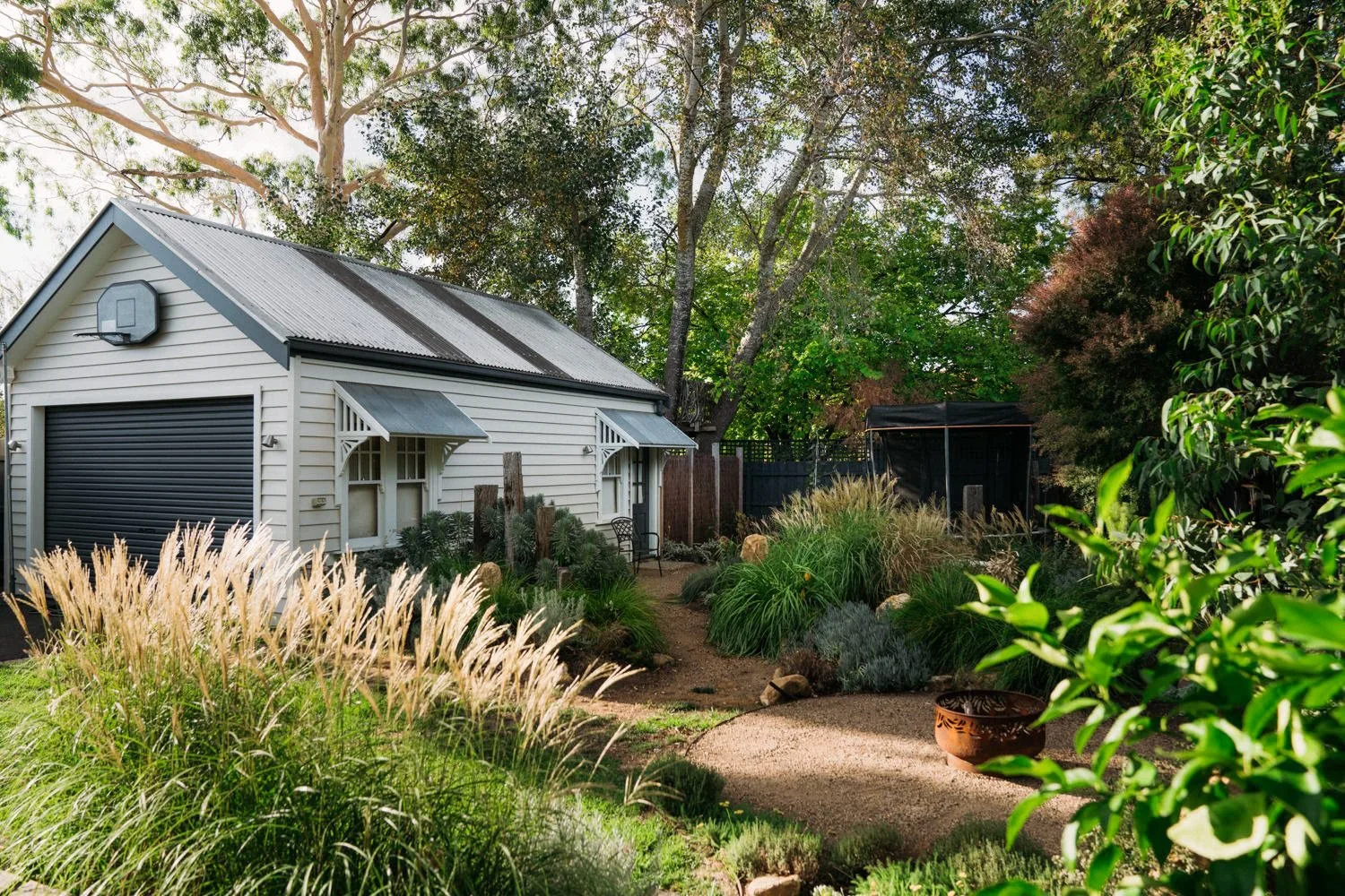 A pale weatherboard house framed by grasses and garden planting in Ringwood.