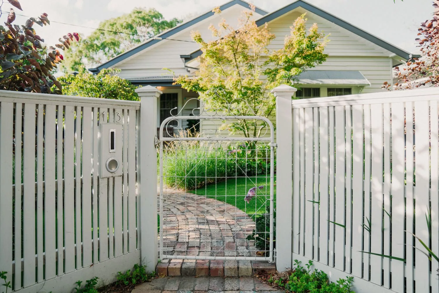 Open white gates lead to a brick garden path.